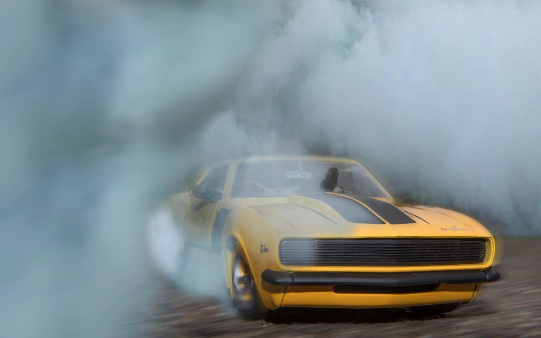 a yellow camaro car drifting in circular motion creating enough friction to produce smoke and tire marks
